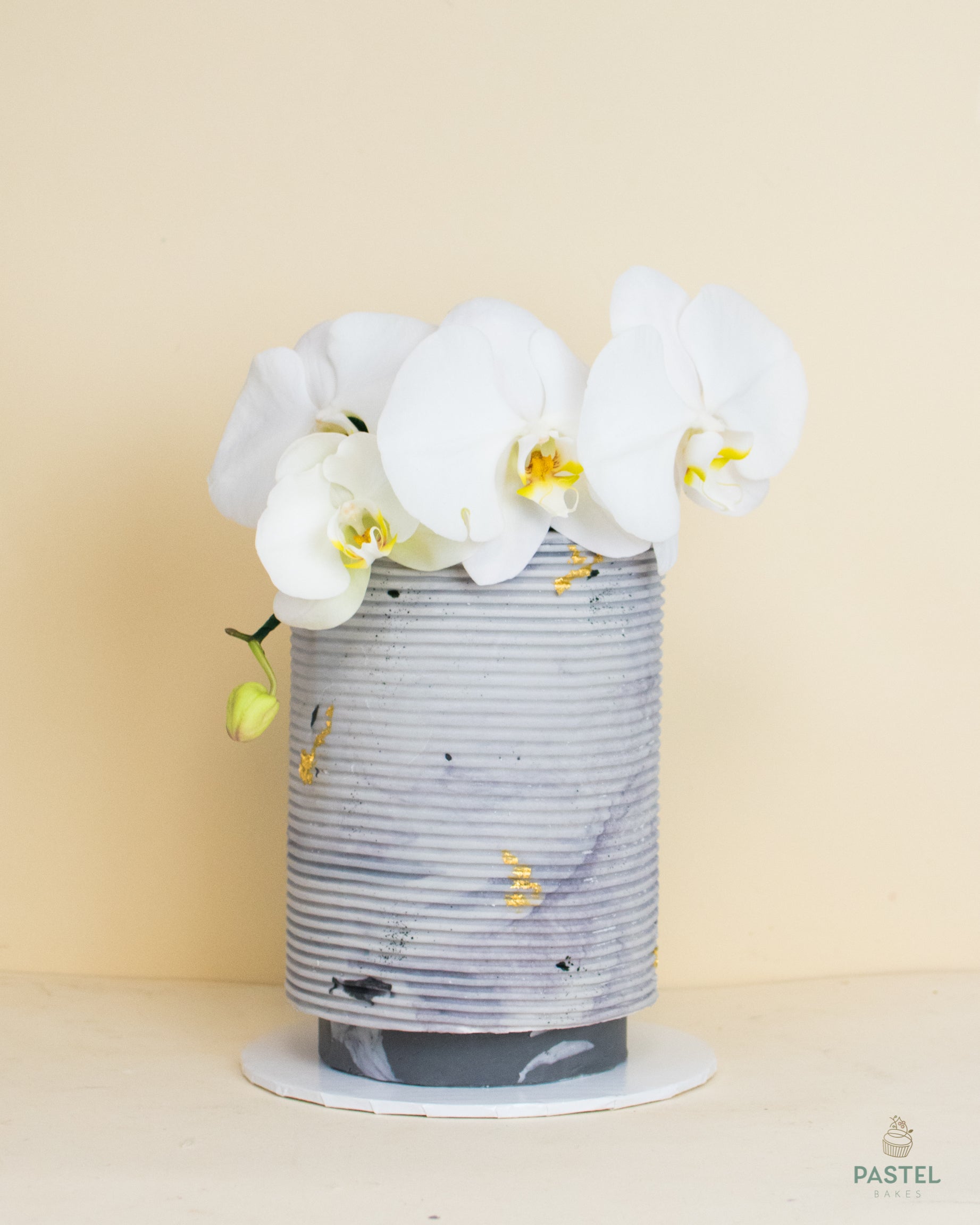 A high light-purple cake with decorative white orchid flowers on top of it.